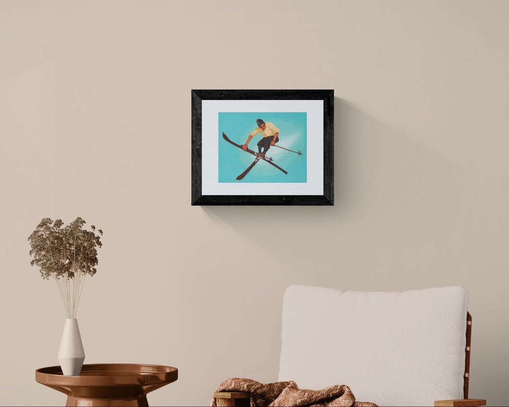 Framed artwork of a skier on a beige wall above a wooden table and chair.
