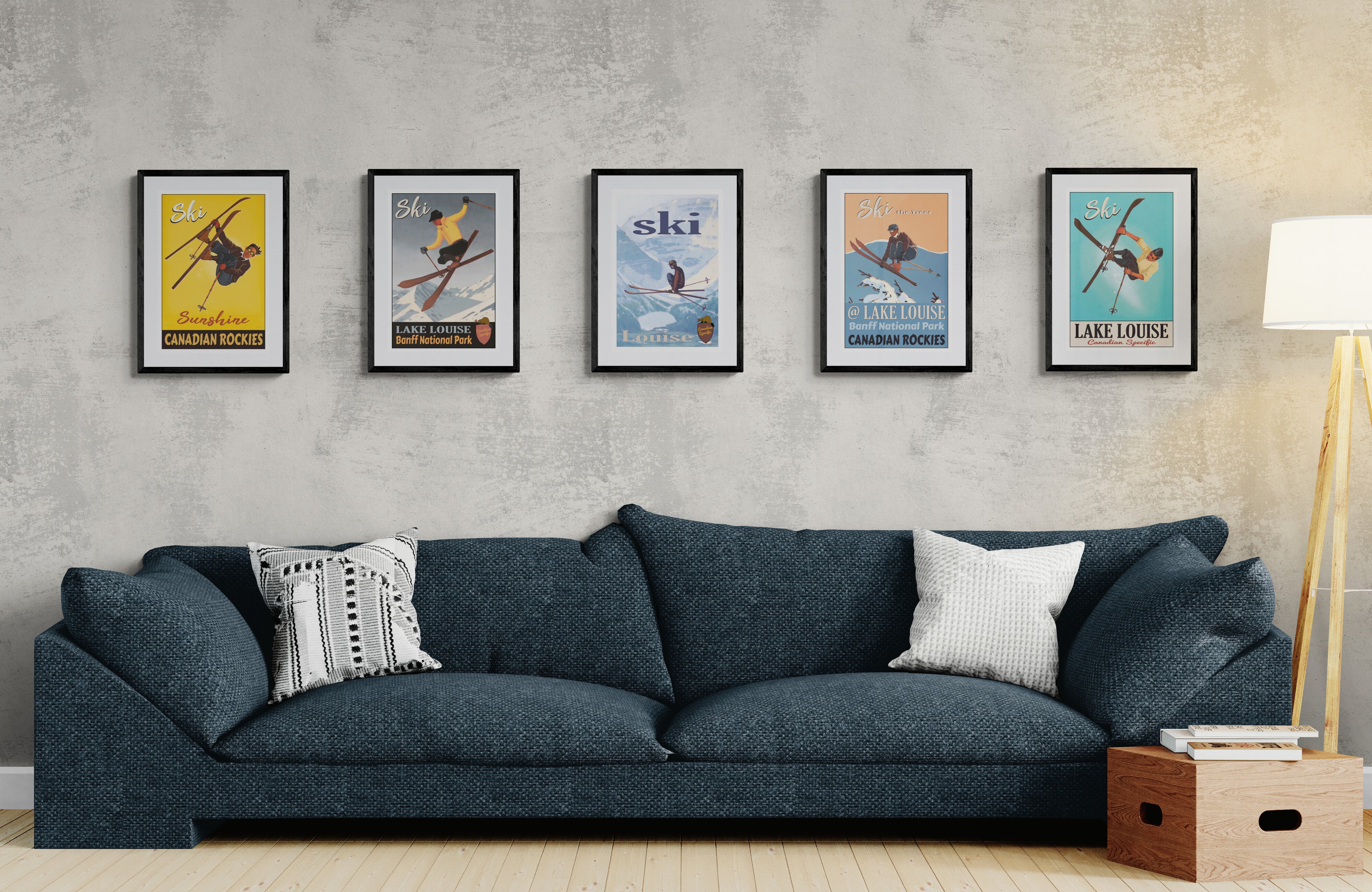 Blue sofa with decorative pillows against a wall, with five framed posters hung on the wall behind, depicting vintage skiers performing various mid-air tricks.