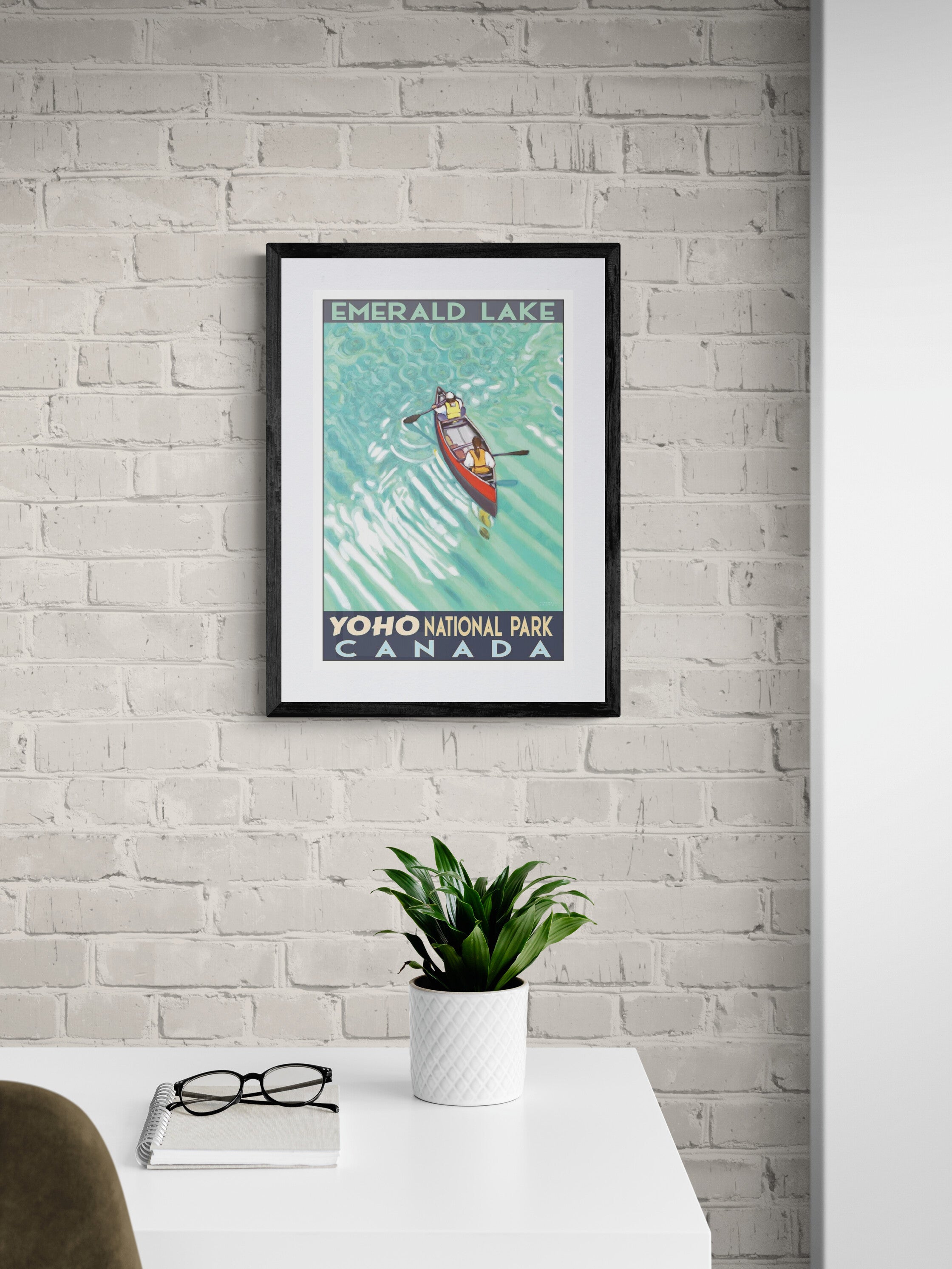 Framed poster of two people canoeing on Emerald Lake, Yoho National Park, Canada on a white brick wall.